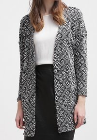 Czarny i biały kardigan w wzory z długimi rękawami i otwartym przodem. Tekstura dzianiny zawiera geometryczne wzory i luźny krój.