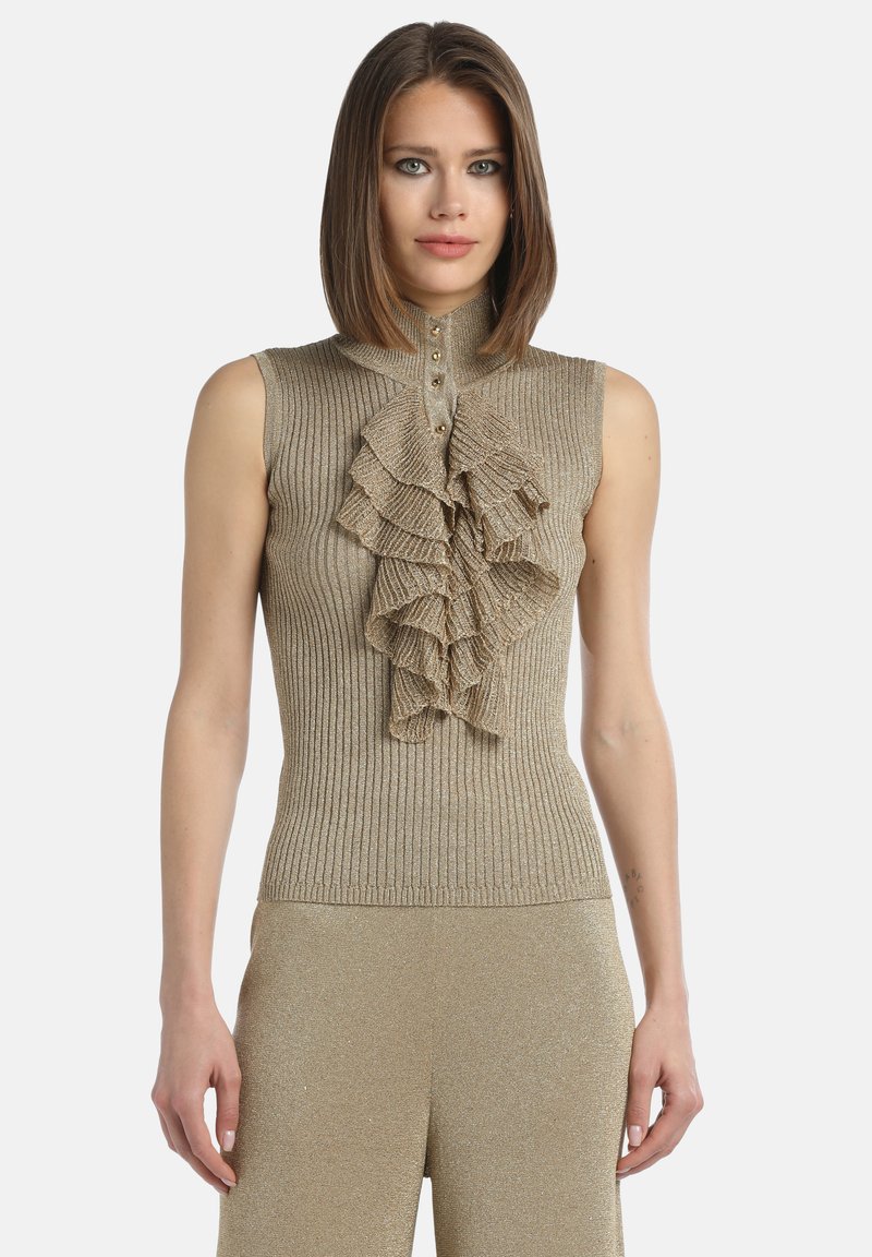 Femeie cu părul drept, brunet, purtând un top fără mâneci, de culoare aurie, cu model cu nervuri și detalii din volane suprapuse pe față.