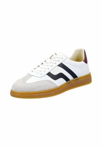 Bílá teniska s semišovou špičkou, černými proužky a hnědým prvkem na patě. Má texturovanou gumovou podrážku a polstrovaný jazyk.