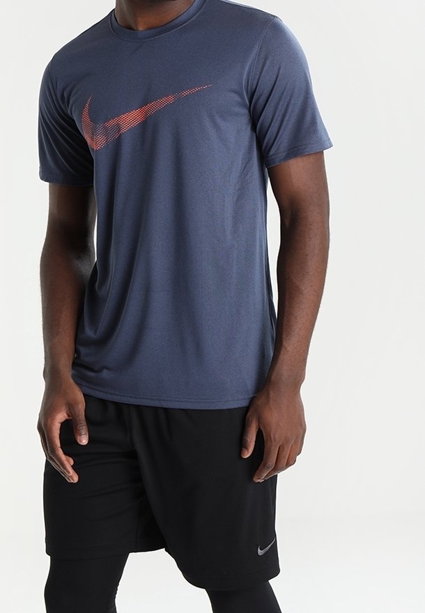 Mörkblå atletisk skjorta i lätt tyg, med en röd Nike swoosh-logotyp på bröstet, tillsammans med svarta shorts.