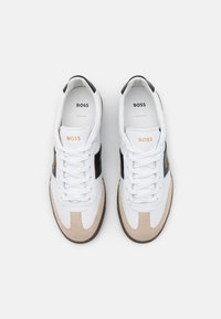 Vita sneakers med beige mockadetaljer, svarta sidospår och texturerad gummisula. Har snörning fram och "BOSS"-märke på insidan.