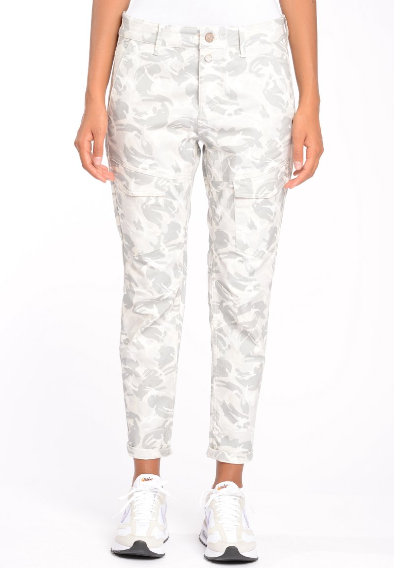 Pantalon cargo camouflage gris clair et blanc avec poches à rabat, porté avec des baskets blanches et un haut blanc, visible de la taille aux chevilles.