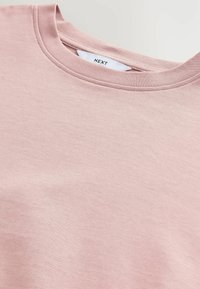 Světle růžová mikina s kulatým výstřihem vyrobená z měkké tkaniny s hladkým povrchem. Vyznačuje se plochou etiketou se jménem značky "NEXT" uvnitř límce.
