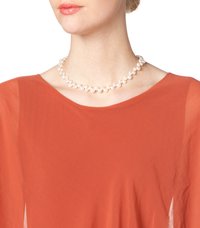 Pearl necklace with white round pearls of varying sizes, strung together, worn over a rust-colored sheer top.