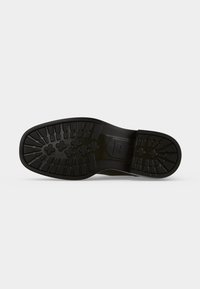 Semelle de chaussure noire avec des rainures profondes présentant un mélange de motifs rectangulaires et en forme de croix à l'avant et au niveau du talon.