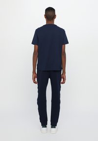 Navy bomulls t-skjorte og matchende joggebukser, med en avslappet passform, korte ermer og elastiske mansjetter. Fullført med hvite sneakers.