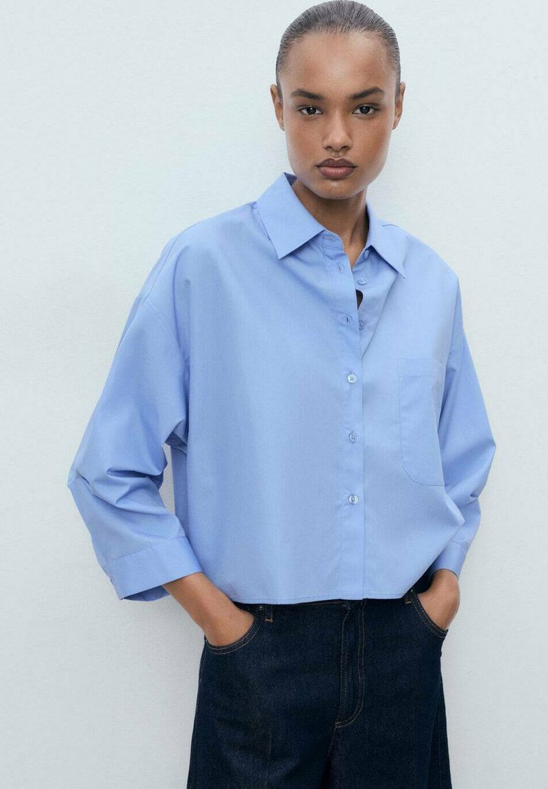 Lichtblauw button-up shirt met een kraag, een borstzak, en driekwart mouwen, gecombineerd met donkere spijkerbroeken.
