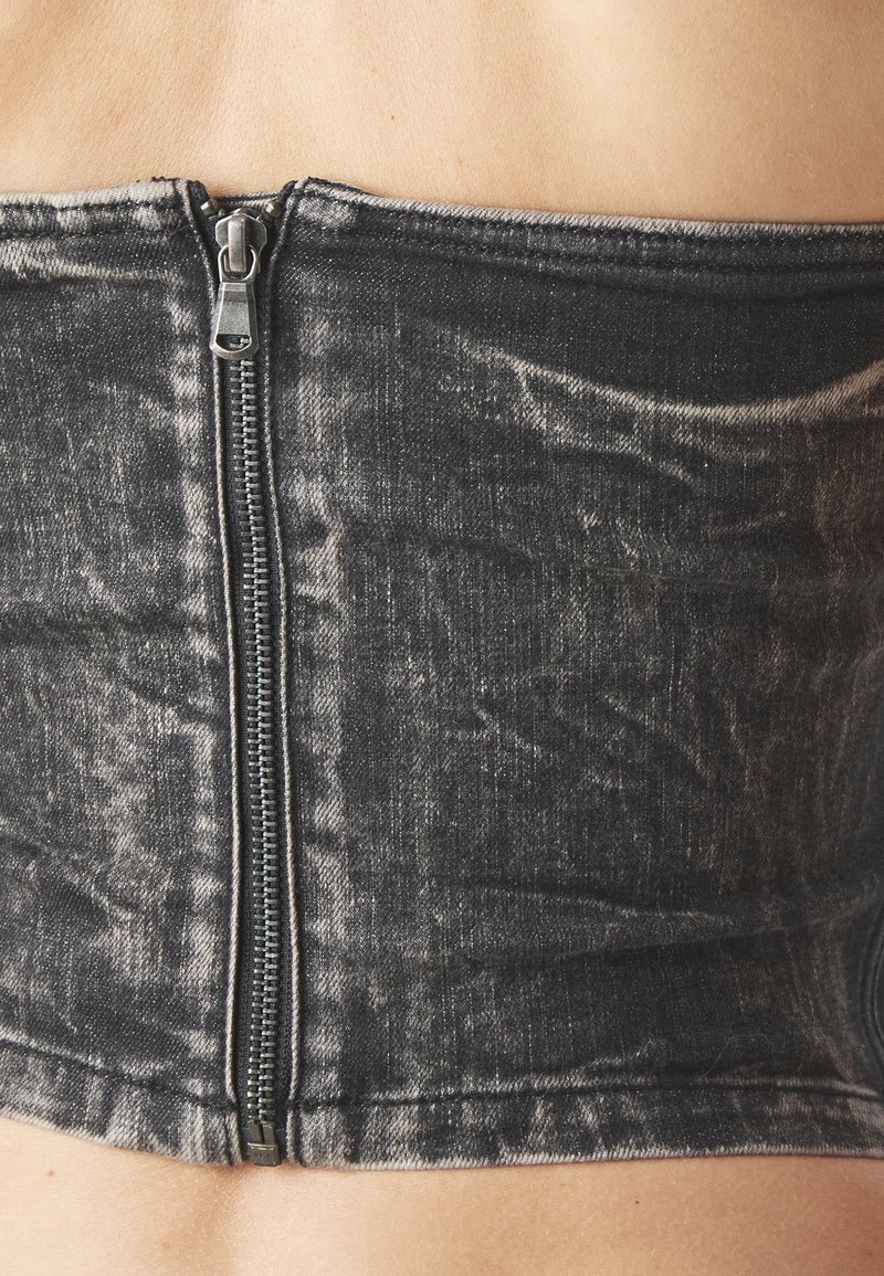 Svart denim korsett-top med dragkedja framtill, med en urtvättad textur och en strukturerad passform, som framhäver en slät kant vid fållen.