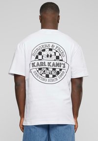 Biely bavlnený tričko s čiernym grafickým potlačou loga jedálne, s kockovanými akcentmi a textom: "BURGER & FRIES," "KARL KANI’S DINER."