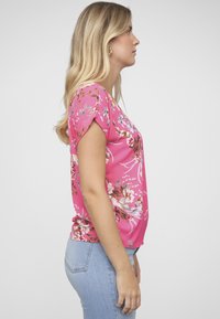 Blusa floral rosa con mangas cortas, textura suave, con patrones de flores multicolores, combinada con jeans ajustados de color azul claro.