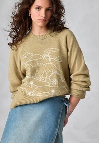 Pulover tricotat bej cu broderie albă a unei munți și a unei case, cu manșete și guler cu nervuri. Combinat cu o fustă din denim albastru deschis.