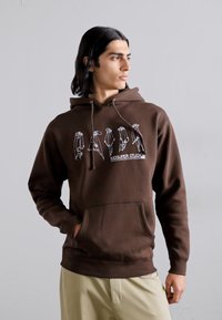 Brown hoodie featuring a graphic design on the chest, drawstrings, a front pocket, and ribbed cuffs. Made from soft fabric.
