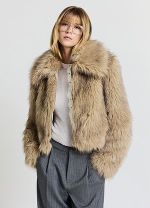 Braune Kunstfelljacke mit breitem Kragen, kurz geschnittenem Design und langen Ärmeln. Trägt man über einem hellen, gerippten Oberteil und kombiniert mit grauen, dünn gestreiften Hosen.