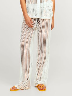 Witte mesh, loszittende broek met een gestructureerd patroon, voorzien van verticale strepen. Gecombineerd met gele slippers. Lichtgewicht materiaal.
