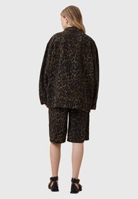 Veste en denim avec imprimé léopard assortie à un short. Les couleurs marron foncé et noir dominent, avec une coupe ample et un design décontracté.