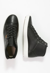 Schwarze Leder-Hochtop-Sneaker mit weißen Gummisohlen, ausgestattet mit einer Schnürung und Metallaugen für zusätzlichen Halt.