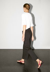 White short-sleeve top paired with high-waisted black wide-leg pants and red flat sandals. Smooth texture and minimalist design.