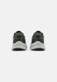 Zapatillas deportivas negras y verdes con una parte superior texturizada, suela de color gris claro en contraste y detalles reflectantes. Lengüeta en el talón para facilitar el uso.
