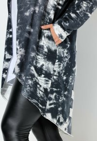 Zwart-wit tie-dye cardigan met een asymmetrische zoom, gemaakt van een textuurstof en voorzien van een zak. Gepaard met zwarte legging.