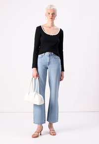 Svart langermet topp med hvit kant, lyseblå vide jeans, brune hælsandaler og en hvit håndbag. Glatt stofftekstur gjennom hele.