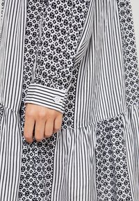 Robe noire et blanche avec tissu à rayures et motifs géométriques, dotée d'un poignet à boutons et d'une jupe plissée pour un effet texturé.