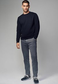 Marinblå sweatshirt, grå jeans och svarta sportskor med vita detaljer. Slim fit och rundad halsringning, textil med minimal detaljering.