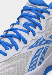 Λευκό αθλητικό παπούτσι από διχτυωτό υλικό με φωτεινά μπλε κορδόνια και λογότυπο, κοντινή λήψη που δείχνει την λεπτομερή υφή και ραφές.