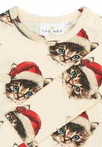 Long-sleeve top featuring a cream fabric with a textured finish, adorned with repeated images of kittens wearing red Santa hats.
