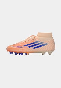 Botín de fútbol naranja con rayas azules, parte superior texturizada y un cuello alto. Presenta tacos cónicos y un talón reforzado.