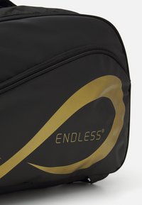 Schwarze Sporttasche mit einem goldenen Wellenmuster und dem Wort "ENDLESS" in einer modernen Schriftart; aus strapazierfähigem, strukturiertem Stoff.