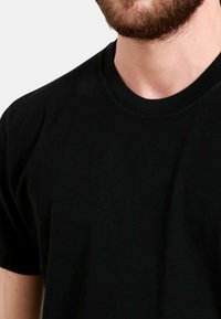 T-shirt in cotone nero con collo rotondo, maniche corte e una texture liscia, che mostra solo i dettagli della parte superiore del corpo e del collo.
