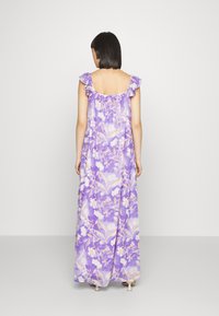 Vestido maxi em estampado floral lavanda, com alças com babados, um design fluido e costas arredondadas. Tecido leve com cores vibrantes.