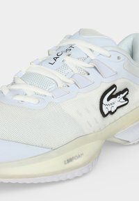Λευκό αθλητικό παπούτσι Lacoste με λευκά κορδόνια, πλέγμα πάνω μέρος, μαύρο λογότυπο κροκοδείλου στο πλάι και την ένδειξη «LSRFOAM» στην σόλα.