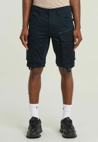 Bermuda cargo blu navy con più tasche, dettagli con zip, orli regolabili e un tessuto resistente. Indossate con sneaker nere e calze bianche.