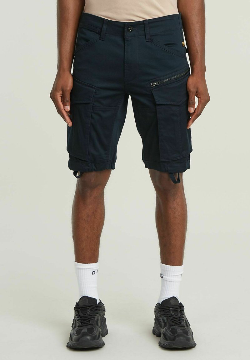 Bermuda cargo blu navy con più tasche, dettagli con zip, orli regolabili e un tessuto resistente. Indossate con sneaker nere e calze bianche.