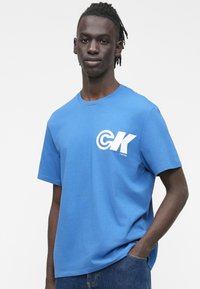 Μπλε βαμβακερό μπλουζάκι με κοντά μανίκια, στρογγυλή λαιμόκοψη και λευκό λογότυπο CK μπροστά. Ομαλή υφή και άνετη εφαρμογή.