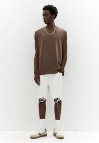 Brown sleeveless top, distressed white shorts, beige and brown sneakers, and a silver chain necklace. Stand on a plain background.