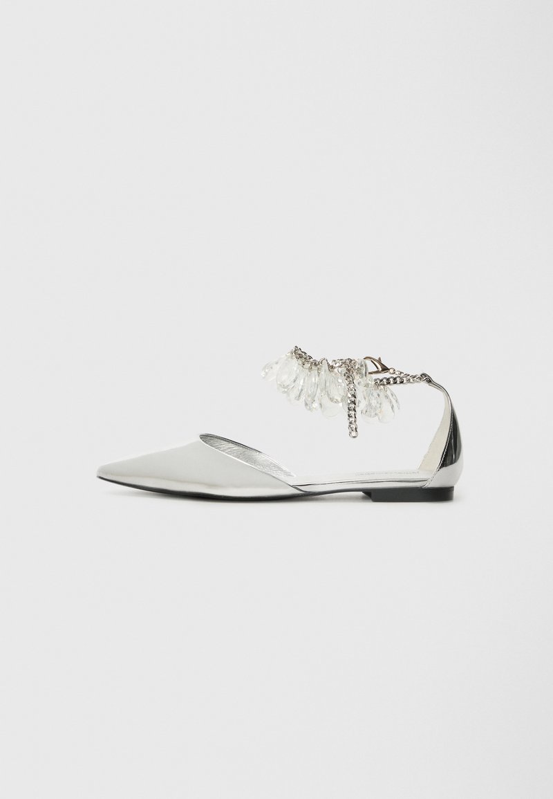 Scarpa flat argentata con punta affusolata, dettagli metallici e cinturino decorativo alla caviglia con perline trasparenti e catena. Superficie liscia e lucida.