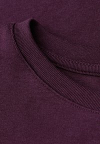 Burgundská bavlněná látka s hladkým, strukturovaným povrchem. Má kulatý výstřih s žebrovanými okraji a mírnou elasticitu.