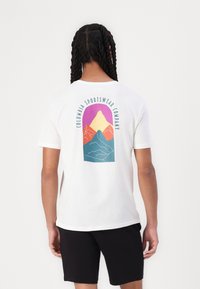 Camiseta blanca de algodón con un gráfico colorido de montaña en la parte posterior, con el texto "Columbia Sportswear Company" curvado arriba.