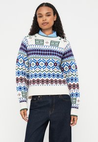 Maglione lavorato a maglia in crema con motivi geometrici multicolori in blu, verde e bordeaux. Presenta un orlo e polsini a coste.
