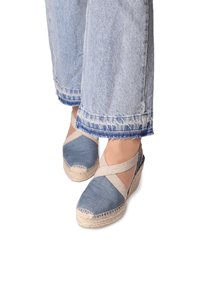 Cuñas de espadrille de tela azul con suela de yute, que presentan correas beige entrelazadas y una punta redondeada. Textura de denim evidente en el material.