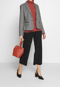 Grå mønstret blazer, rød turtleneck, sorte culottes og sorte spidse slingback hæle. Holder en lille rød lædertaske med ringehåndtag.