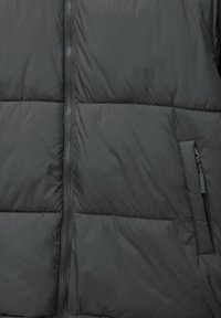 Mustap padded-takki, jossa on tilkkutäkki-kuviointi, keskeinen vetoketju ja sivutasku vetoketjusulkimella. Sujuva, kevyt materiaali.