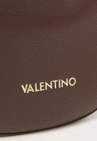 Brun lærveske med strukturert overflate og et gull "Valentino"-logo preget på forsiden. Rund form med minimale detaljer.