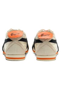 Beżowe zamszowe sneakersy z czarnymi akcentami i pomarańczowymi paskami na pięcie. Posiadają teksturowaną cholewkę, gumową podeszwę oraz logo Tygrysa na pięcie.