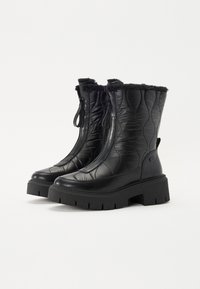 Bottes en cuir matelassé noires avec des poignets en fausse fourrure, des zippers latéraux et des semelles en caoutchouc chunky présentant un motif de grip texturé.