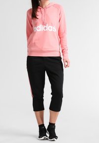 Rosa huvtröja med vit "adidas"-logga, tillsammans med svarta korta sweatpants med röd sidostripa. Bärs med svarta träningsskor.