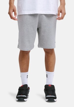 Szare bawełniane szorty sportowe o luźnym kroju, z bocznymi kieszeniami i wykończeniem tuż nad kolanem, zestawione z czarnymi trampkami i białymi skarpetkami.