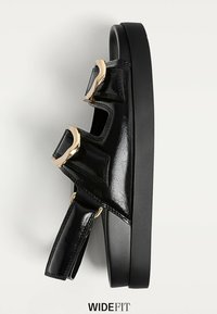 Sort lakerede sandal med tykk sål, to justerbare stropper og guldfarvede metalliske detaljer. Har et bredt fit-design og teksturerede detaljer.
